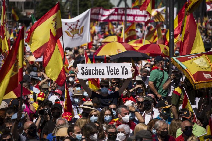 Un hombre con un cartel en el que se lee: `Sánchez vete ya´, entre una multitud de personas con banderas de España. (Foto: Alejandro Martínez Vélez / Europa Press)