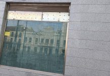 El edificio del Ayuntamiento de Guadalajara, reflejado en la cristalera de un local sin uso de la Plaza Mayor el 5 de junio de 2023. (Foto: La Crónic@)