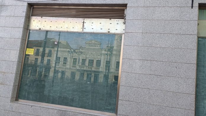 El edificio del Ayuntamiento de Guadalajara, reflejado en la cristalera de un local sin uso de la Plaza Mayor el 5 de junio de 2023. (Foto: La Crónic@)