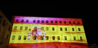 La bandera de España cubre todo un edificio de Toledo Bandera de España sobre la fachada de las Cortes de Castilla-La Mancha.